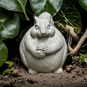 May include: A grey concrete squirrel statue with a rounded belly and a bushy tail. The squirrel is holding a nut in its paws and has a sweet expression on its face.