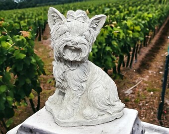 May include: A white ceramic figurine of a Yorkshire Terrier dog sitting on a white pedestal. The figurine is detailed with fur and a bow.