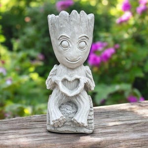 May include: A gray concrete garden statue of a character holding a heart in its hands. The statue is sitting on a wooden surface.