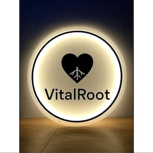 May include: Round, illuminated sign with a black heart and tree graphic inside a white circle. The text "VitalRoot" is below the heart. The sign has a black border and emits a soft, warm light.