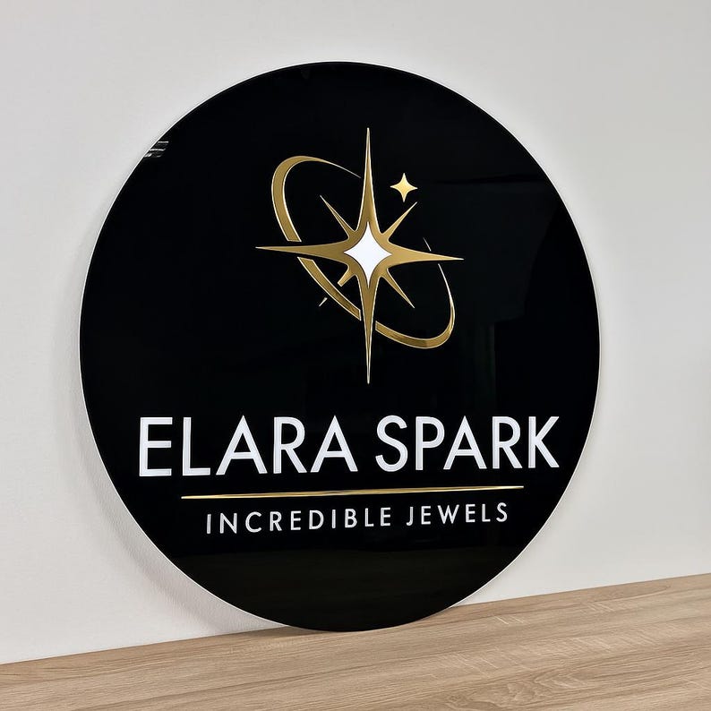 May include: A round, black sign with the words "ELARA SPARK" in white, and "INCREDIBLE JEWELS" in gold. The sign features a gold and white starburst logo. The sign is displayed on a wooden surface.