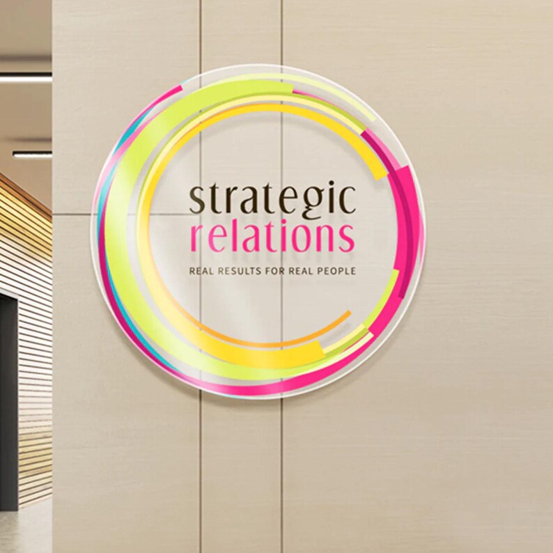 May include: A circular sign with a colorful abstract design and the text "strategic relations" in black font. The text "real results for real people" is in smaller black font below the main text.