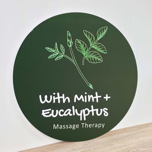 May include: A green circle with a white outline and the text "With mint + Eucalyptus" and "Massage Therapy" in white. A green line drawing of a sprig of mint and eucalyptus leaves is above the text.