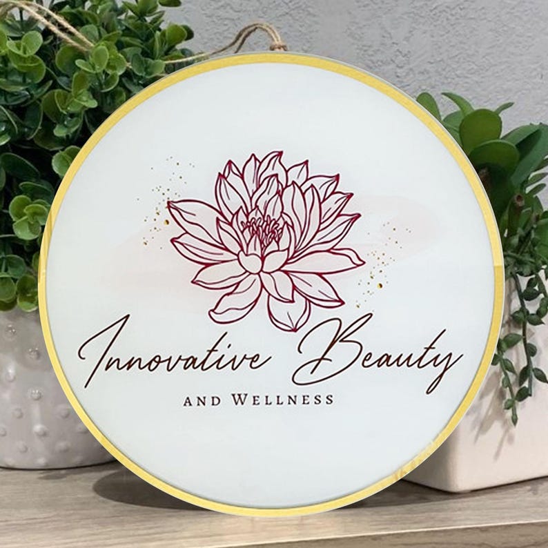 May include: A white round sign with a gold border. The sign has a red floral design and the text "Innovative Beauty and Wellness".