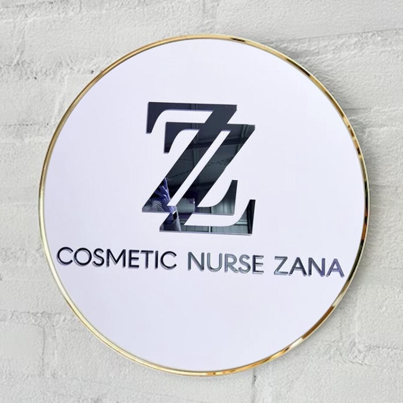 May include: A white round sign with a gold border. The sign has a black logo with the letters "ZZ" and the text "COSMETIC NURSE ZANA".