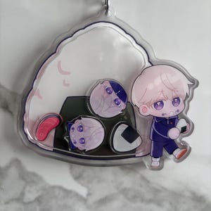 May include: A clear acrylic keychain featuring anime-style illustrations. The design includes a character in a blue uniform, holding an onigiri, and several onigiri with anime faces. The keychain is attached to a silver chain.
