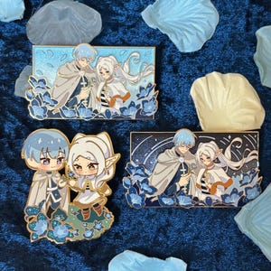 May include: Four enamel pins featuring anime-style characters with blue and white hair, wearing capes and holding hands. The pins are set against a background of blue flowers and a starry night sky. The pins are rectangular and have gold borders.