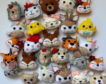 May include: A collection of felt animal hair clips, including a hedgehog, bunny, bear, lamb, fox, deer, and tiger. Each clip is hand-stitched with detailed features and colorful accents, such as flowers and bows. These clips are ideal for children.