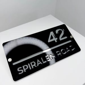May include: A black rectangular address sign displaying the number "42" and the words "SPIRALEN ROAD" in silver lettering. The sign is fixed with two silver screws. The website "Spiralen.ee" is printed at the bottom.