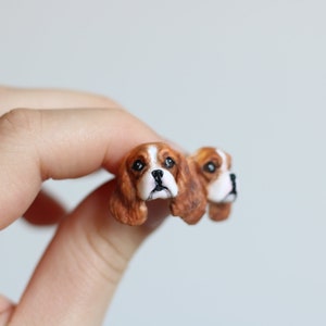 Peut inclure: Une paire de boucles d'oreilles en argile polymère faites à la main représentant des têtes de chiens Cavalier King Charles Spaniel. Les boucles d'oreilles sont brunes, blanches et noires.