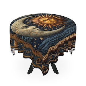 Puede incluir: Mantel redondo con un diseño celestial. Presenta una luna creciente, un sol y estrellas en dorado y crema sobre un fondo azul oscuro. La mesa tiene patas negras y un borde blanco.