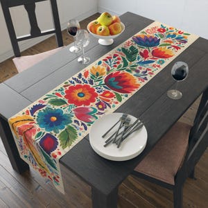May include: A colorful floral table runner with a cream background. The runner features large, vibrant flowers in red, blue, yellow, and orange. The table is set with plates, silverware, and wine glasses, creating a festive dining scene.