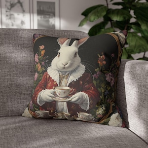 Puede incluir: Un conejo blanco con una chaqueta roja y dorada con un cuello de encaje blanco sostiene una taza de té y un platillo. El conejo está rodeado de flores y vegetación sobre un fondo oscuro.