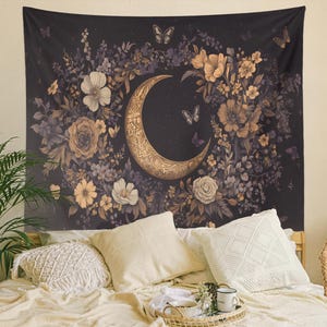 May include: A tapestry featuring a gold crescent moon surrounded by a wreath of stylized flowers and butterflies on a dark background.