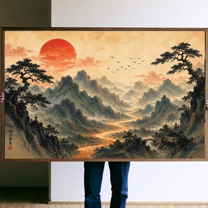 May include: A framed landscape painting featuring a large red sun over misty mountains, a winding river, and pine trees. A small figure stands on a cliff edge on the left. The artwork includes black ink calligraphy and a red seal in the lower left corner.