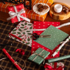 Könnte beinhalten: Miniatur-Weihnachtsszene mit verpackten Geschenken, Geschenkpapier und einem Kamin. Rote und grüne Geschenkboxen sind mit silbernem Band und Bindfaden gebunden. Geschenkpapier zeigt Stechpalmen- und Schneeflockenmuster. Ein Teller mit Keksen und eine Tasse sind ebenfalls vorhanden.