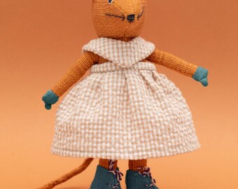 Könnte beinhalten: Eine braune und orangefarbene Stoffmauspuppe, die ein weiß-braunes Gingham-Kleid und blaue Schuhe trägt. Die Maus hat einen langen Schwanz und rosa Ohren.