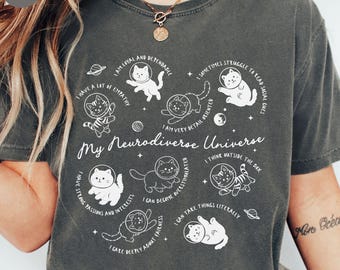 May include: Dark gray t-shirt with the text "My Neurodiverse Universe" and illustrations of cats in space suits. The shirt features phrases like "I have a lot of empathy" and "I can take things literally."