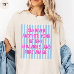 May include: Ivory-colored t-shirt with the text "Survived Another Year of IEPs, Behaviors, and Pure Magic" in pink and blue. The text is centered within a blue striped rectangle.