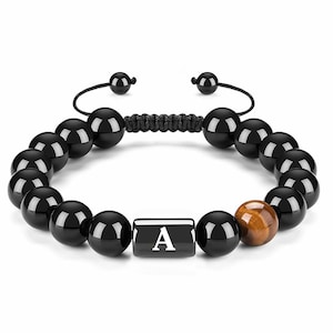 May include: Black beaded bracelet with a sliding knot closure. The bracelet features large, glossy black beads, a single brown tiger eye bead, and a black rectangular bead with the letter "A".