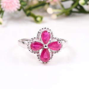 Könnte beinhalten: Ein silberner Ring mit einem pinkfarbenen Rubinblüten-Design. Die Blume hat fünf Blütenblätter, jedes mit einem birnenförmigen Rubin.