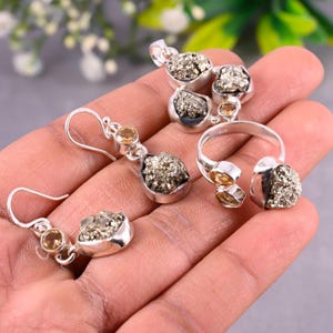 May include: A set of silver jewelry featuring pyrite and citrine gemstones. The set includes a pendant, a pair of earrings, and a ring.