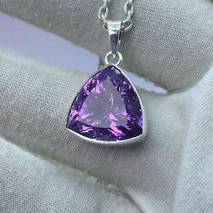 May include: A silver chain necklace with a triangular amethyst pendant. The amethyst is a deep purple color and has a faceted cut.