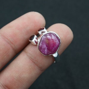 May include: A silver ring with a large, faceted, pink ruby gemstone and two smaller ruby accents.