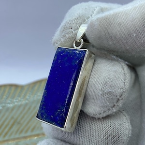 May include: A silver pendant featuring a rectangular lapis lazuli stone. The stone is a deep blue colour with white veins.