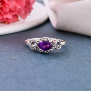 May include: A silver ring with a purple oval gemstone surrounded by smaller clear gemstones.