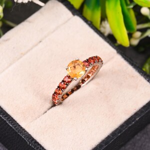 May include: A silver ring with a round orange gemstone surrounded by smaller red gemstones.