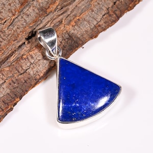 Puede incluir: Un colgante de plata con una piedra preciosa de lapislázuli triangular de color azul oscuro. El colgante está engastado en un marco de plata y tiene un acabado pulido.