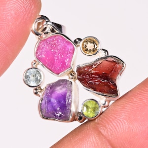 May include: A silver pendant featuring a cluster of raw gemstones. The pendant includes pink, red, purple, green, and yellow stones.