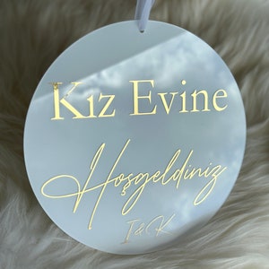 May include: White round acrylic sign with gold lettering that reads "Kız Evine Hoşgeldiniz" and "I&K".