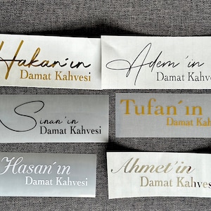 May include: Six rectangular adhesive labels with metallic gold, black, and silver lettering. The labels feature the names Hakan'in, Adem'in, Sinan'in, Tufan'in, Hasan'in, and Ahmet'in, each followed by the text Damat Kahvesi in various fonts.