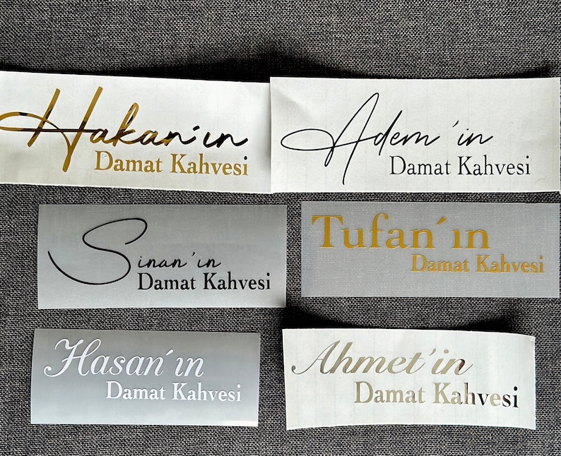 May include: Six rectangular adhesive labels with metallic gold, black, and silver lettering. The labels feature the names Hakan'in, Adem'in, Sinan'in, Tufan'in, Hasan'in, and Ahmet'in, each followed by the text Damat Kahvesi in various fonts.