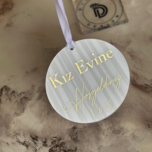 May include: A white round sign with gold lettering that says "Kiz Evine Hosgeldiniz I & E".