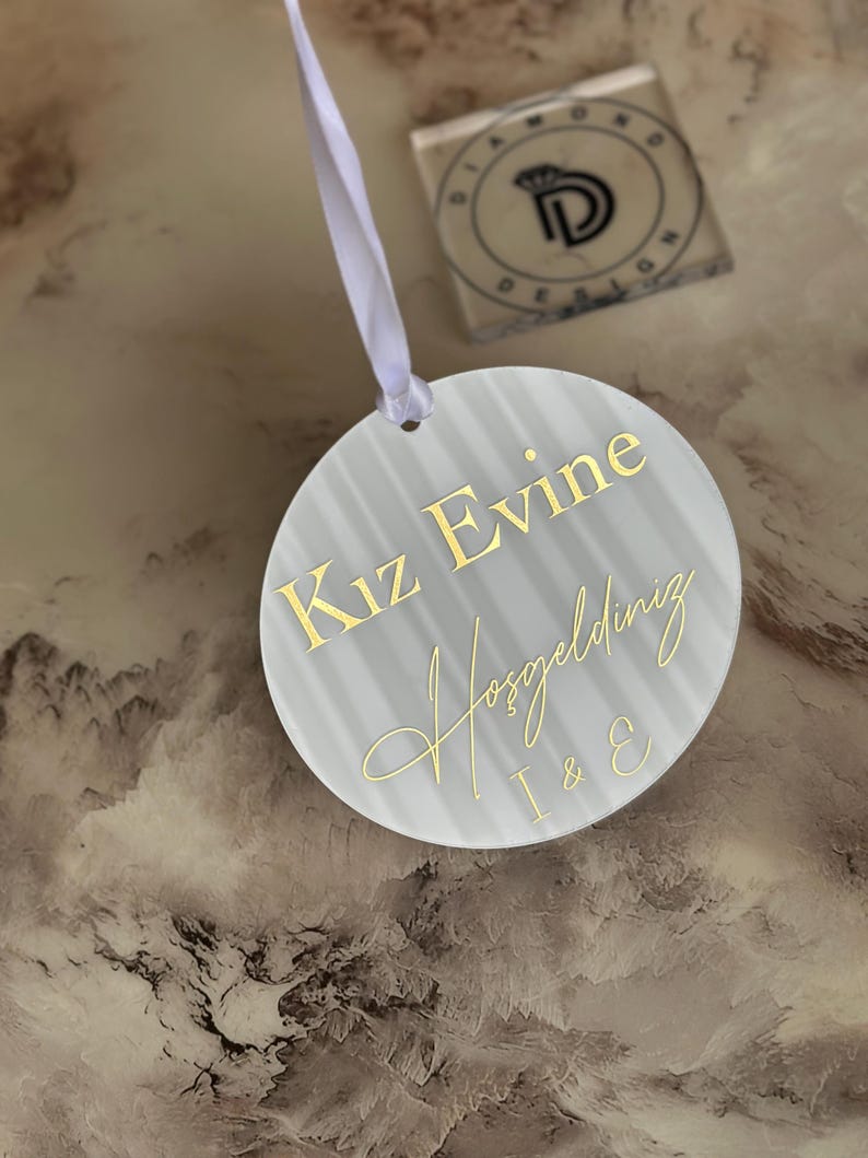 May include: A white round sign with gold lettering that says "Kiz Evine Hosgeldiniz I & E".