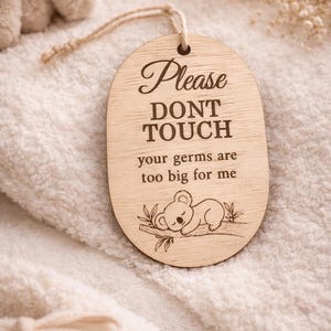 May include: Wooden sign with the text "Please DON'T TOUCH your germs are too big for me". The sign has a koala bear illustration and a string for hanging. The sign is light brown and has a natural wood grain.
