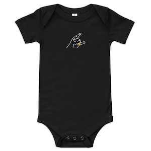 May include: Black baby bodysuit featuring a white outline of a hand in a rock and roll pose, with a gold ring. The bodysuit has short sleeves and poppers at the bottom.