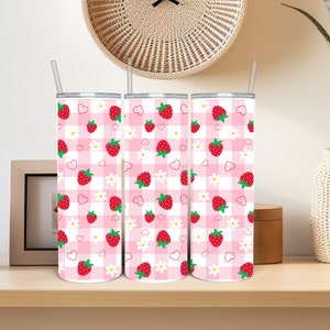 May include: Three stainless steel tumblers with a strawberry pattern. The design features red strawberries, white daisies, and pink hearts on a pink and white gingham background. Each tumbler has a silver lid and a clear straw.