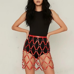 May include: Red leather skirt with a diamond pattern, connected by silver rings. The skirt is worn over a black bodysuit. The model is wearing a black top. The overall look is edgy and stylish.