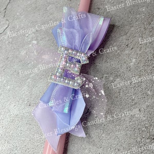 May include: A pink Easter candle with a purple and white ribbon bow and a sparkly letter "E" charm. The candle is decorated with white polka dots and the text "Easter Blessings Candles & Crafts" is repeated throughout the image.