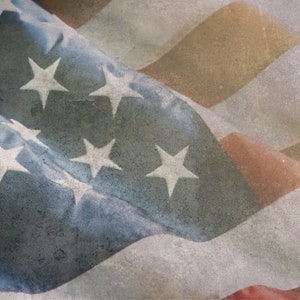 Puede incluir: Un primer plano de una bandera estadounidense descolorida con rayas rojas, blancas y azules. La bandera está arrugada y tiene una superficie texturizada.