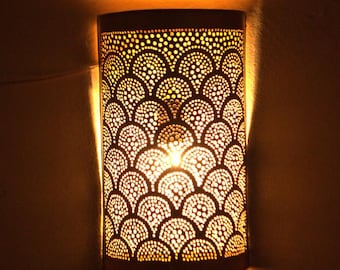 May include: A gold metal wall sconce with a decorative, geometric pattern. The sconce is lit and casting a warm glow.