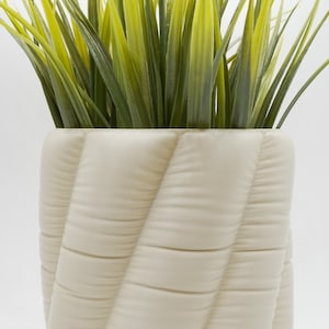 May include: A white ceramic planter with a quilted design, featuring a green leafy plant inside.