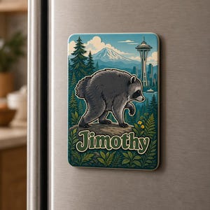 Puede incluir: Un im&aacute;n de nevera rectangular con una ilustraci&oacute;n gr&aacute;fica de un mapache gris de pie sobre una roca. El fondo muestra un bosque, una monta&ntilde;a y la Space Needle. El nombre Jimothy est&aacute; impreso en letras grandes y estilizadas de color verde.