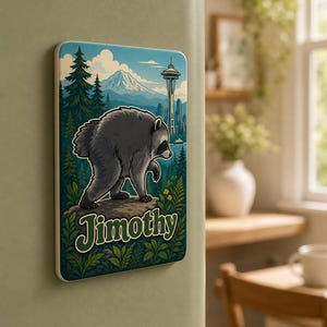 Puede incluir: Un im&aacute;n de nevera rectangular con una ilustraci&oacute;n gr&aacute;fica de un mapache de pie sobre una roca en un bosque. El fondo muestra una monta&ntilde;a y la Space Needle. El nombre Jimothy est&aacute; impreso en letras grandes y estilizadas de color verde.