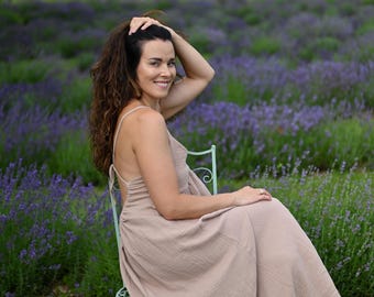 Puede incluir: Un vestido largo de color beige sin mangas, confeccionado en tela texturizada y arrugada, con tirantes finos, diseño de espalda descubierta con lazos y una falda fluida y holgada que llega hasta los tobillos.