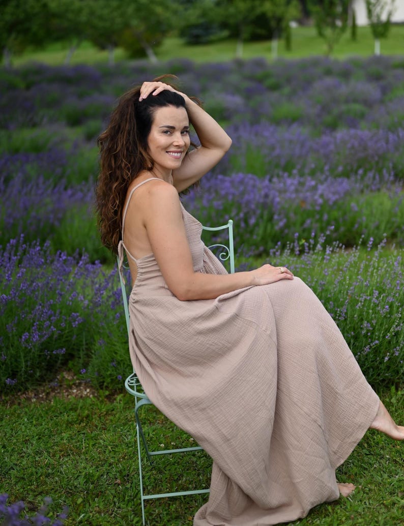 Taupe backless cotton maxi dress with deep V-neckline and open tie back. Made from breathable double gauze muslin, Oeko-Tex certified. Flowy A-line silhouette, perfect for boho bridesmaids, Greek goddess looks, and summer weddings. A lightweight gauze sun dress that’s handmade, easy to pack, and elegant for barefoot moments and garden gatherings.
